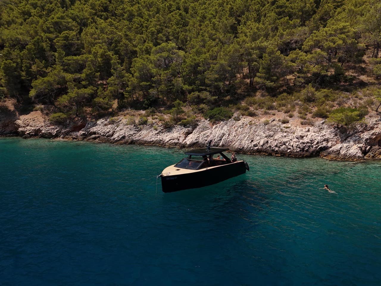 The Colnago 35 at anchor below pine-covered cliffs, swimmer in the foreground